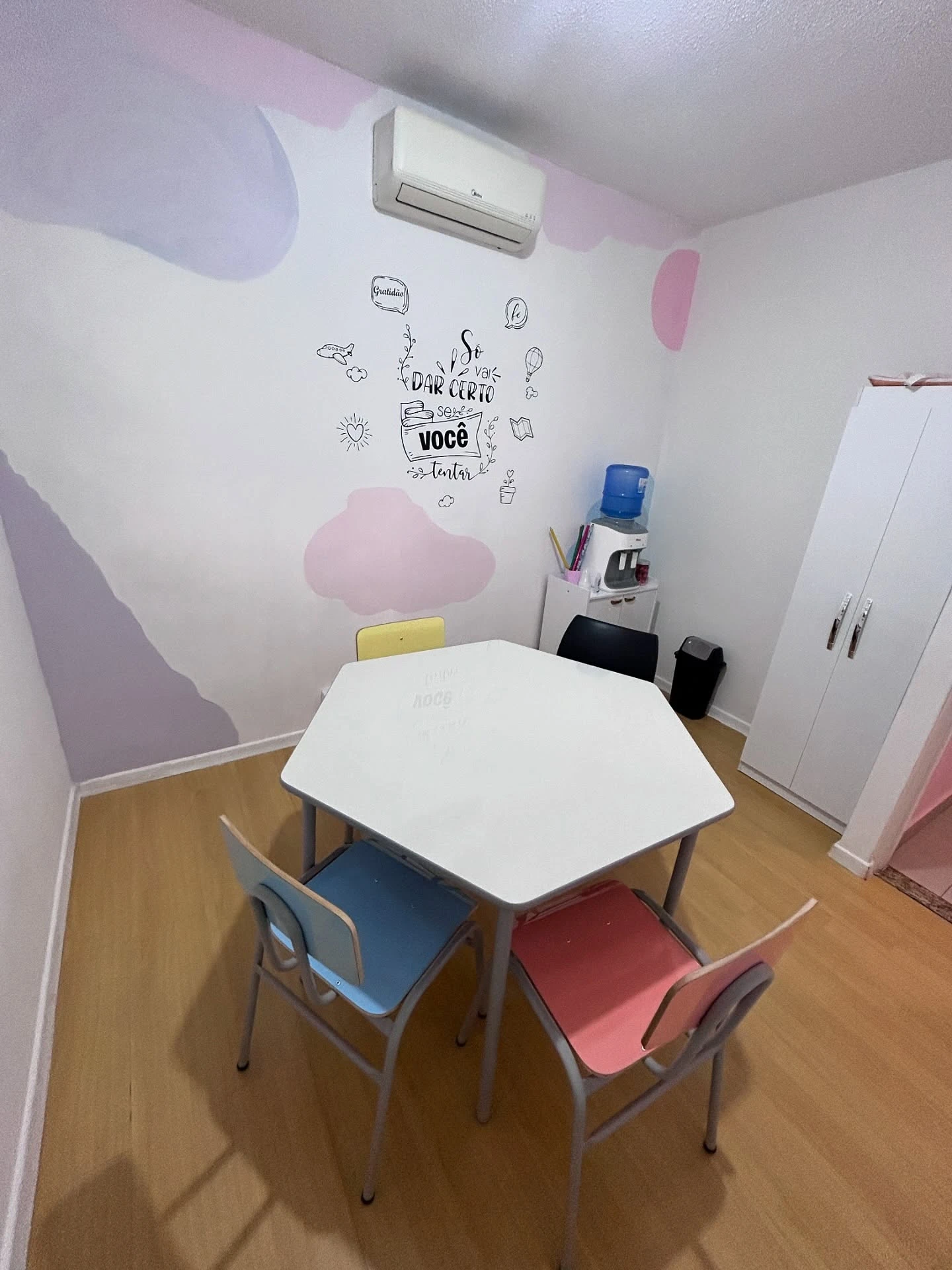 Sala de aula da Prof. Carolina Raiser, ambiente colorido e acolhedor com mesa ampla, ar-condicionado e bebedouro